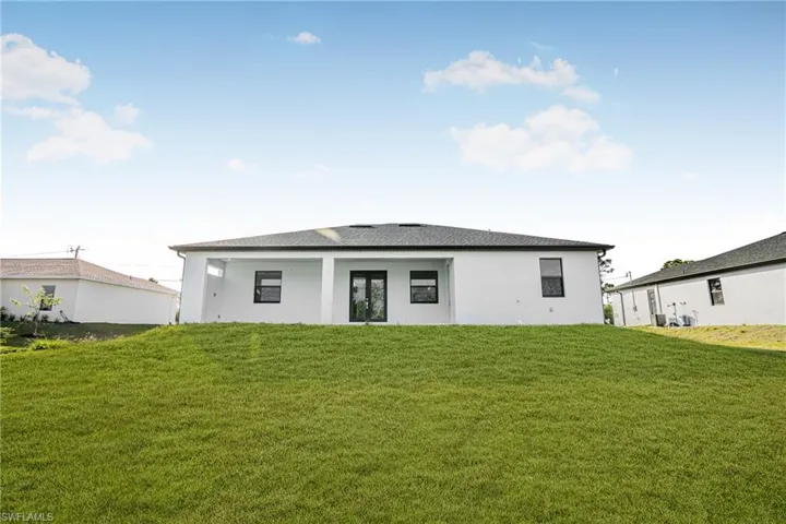 Back of property featuring a yard, stucco siding, roof with shingles, and a patio
