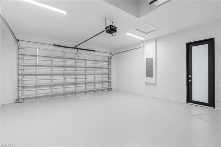 Garage with a textured wall, electric panel, and a garage door opener