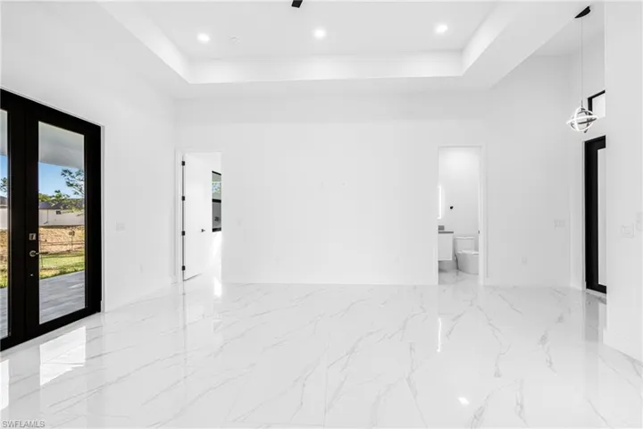 Spare room with a raised ceiling, light marble finish flooring, french doors, and recessed lighting