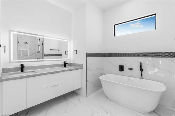 Full bathroom featuring double vanity, a freestanding bath, light marble finish flooring, a marble finish shower, and tile walls