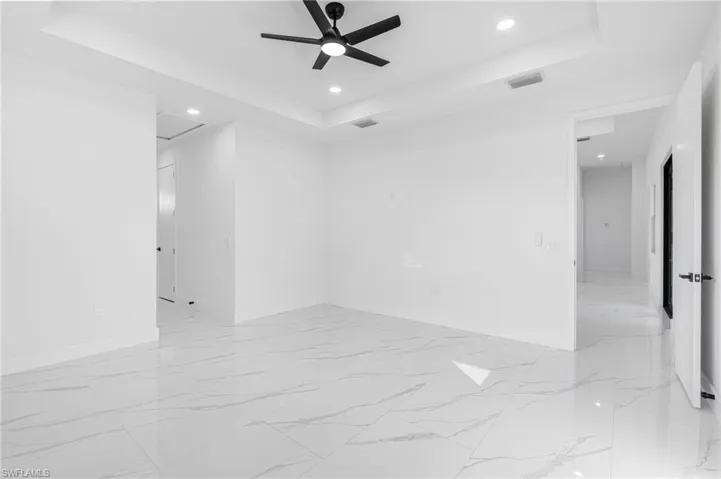 Unfurnished room featuring a tray ceiling, recessed lighting, a ceiling fan, and light marble finish flooring