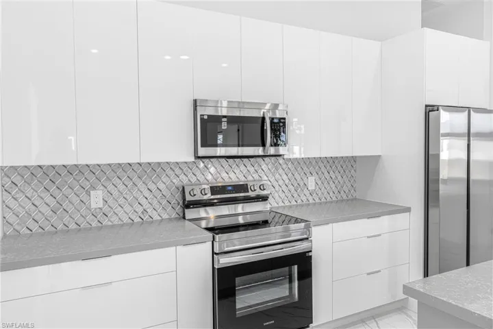 Kitchen with modern cabinets, stainless steel appliances, white cabinetry, and light stone countertops