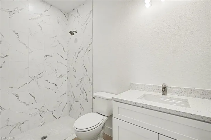 Full bath with vanity, a marble finish shower, and a textured wall