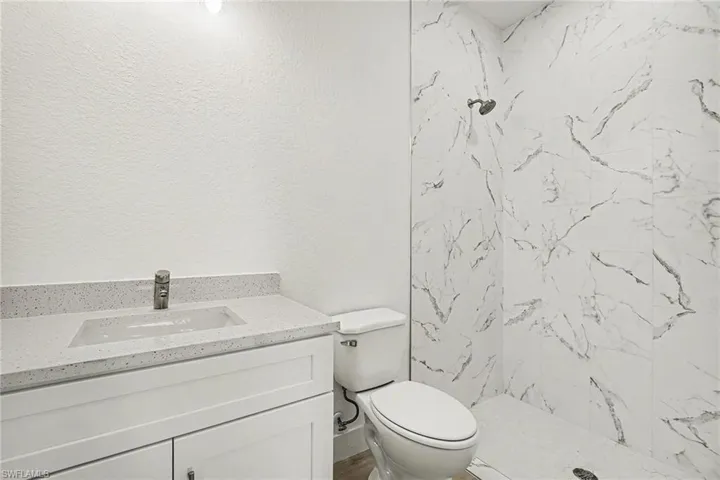 Full bathroom featuring vanity, a marble finish shower, and a textured wall