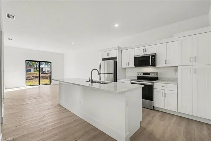 Kitchen featuring stainless steel appliances, white cabinets, an island with sink, light wood-style floors, and recessed lighting