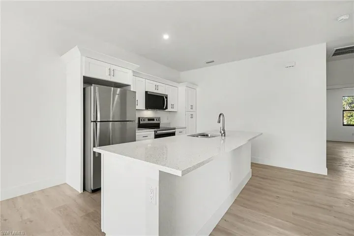 Kitchen featuring stainless steel appliances, white cabinetry, light stone counters, a center island with sink, and light wood-style floors