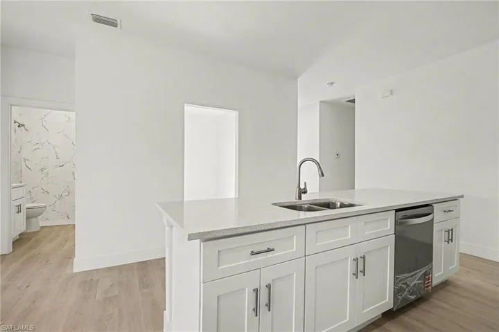 Kitchen with light wood-style floors, white cabinets, light stone countertops, an island with sink, and dishwasher