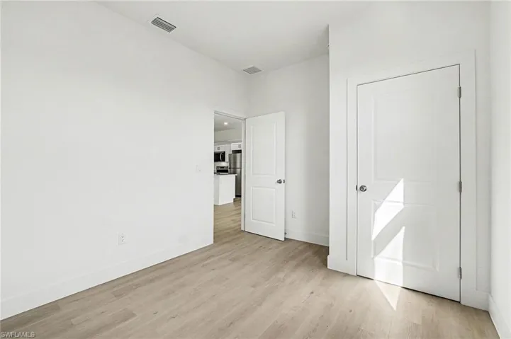 Unfurnished bedroom featuring light wood finished floors and freestanding refrigerator