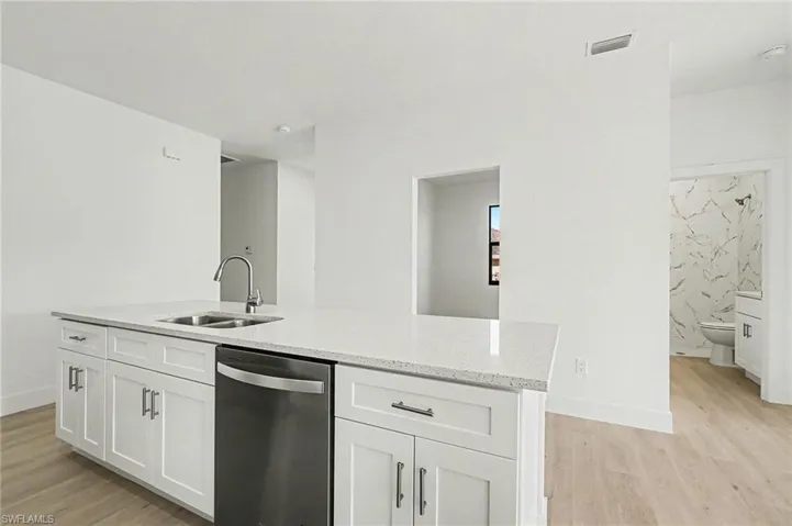 Kitchen featuring stainless steel dishwasher, an island with sink, light wood-style flooring, and light stone counters