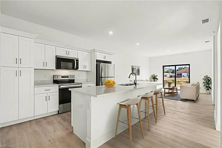 Kitchen with stainless steel appliances, white cabinetry, a breakfast bar area, light wood finished floors, and a center island with sink