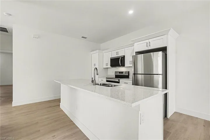 Kitchen with white cabinetry, stainless steel appliances, light wood-type flooring, and a kitchen island with sink
