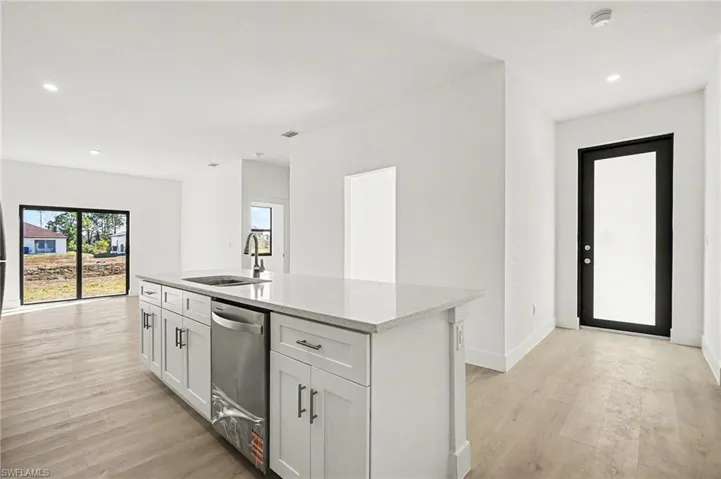 Kitchen with recessed lighting, a kitchen island with sink, dishwasher, light wood finished floors, and light stone countertops