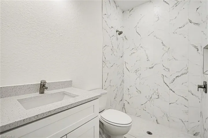 Bathroom with vanity, a textured wall, and a marble finish shower