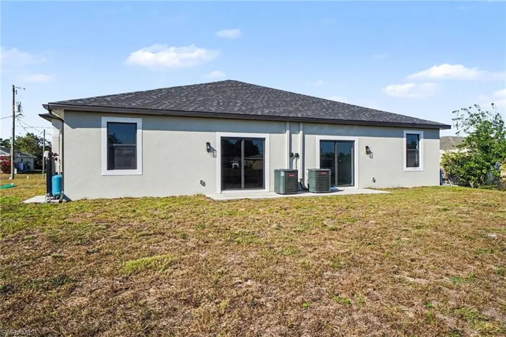 Rear view of house featuring a lawn, stucco siding, roof with shingles, and a patio area