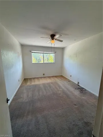 Spare room with light carpet, a ceiling fan, and baseboards