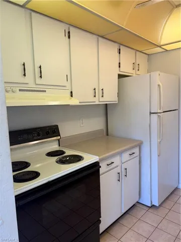Kitchen featuring stove, range hood, light countertops, light tile patterned floors, and fridge