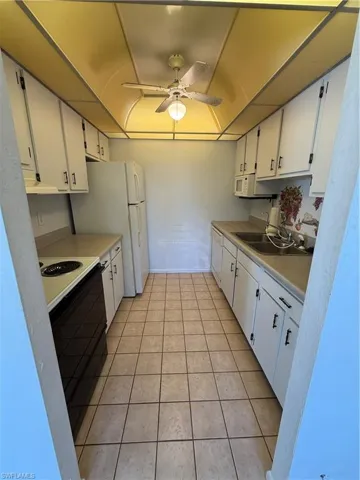 Kitchen with a sink, white cabinetry, stove, ceiling fan, and light tile patterned floors