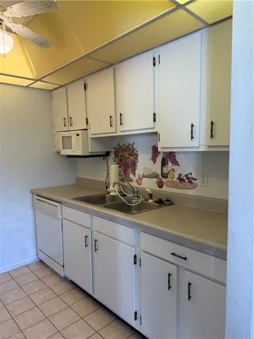 Kitchen featuring light countertops, a sink, light tile patterned flooring, white cabinetry, and dishwasher