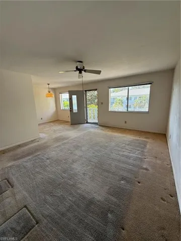 Unfurnished living room with ceiling fan, light carpet, a healthy amount of sunlight, and baseboards