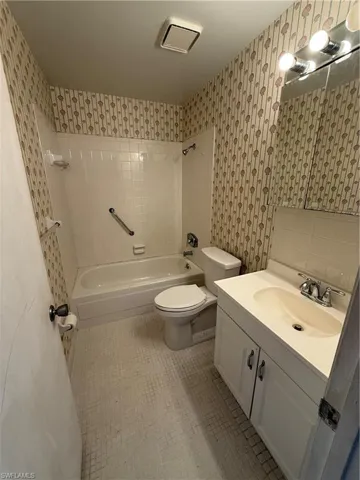 Full bath with tile patterned floors, toilet, wallpapered walls, shower / bath combination, and vanity