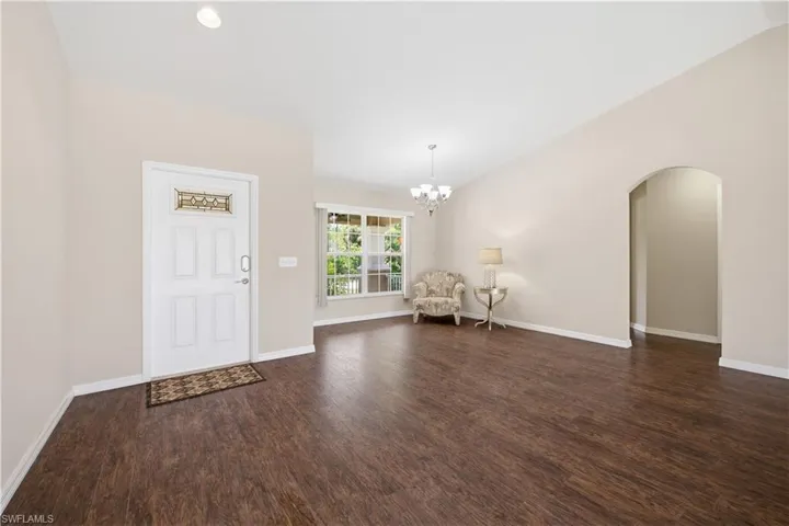 Inviting entryway featuring a white paneled door with decorative glass, vaulted ceilings, and wood-finish flooring