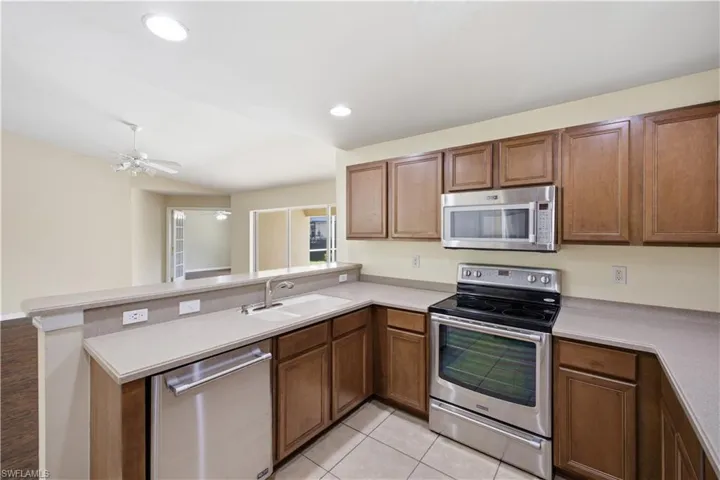 Kitchen featuring wood cabinetry, light-toned countertops, tile flooring, and stainless steel appliances including a range, microwave, and dishwasher