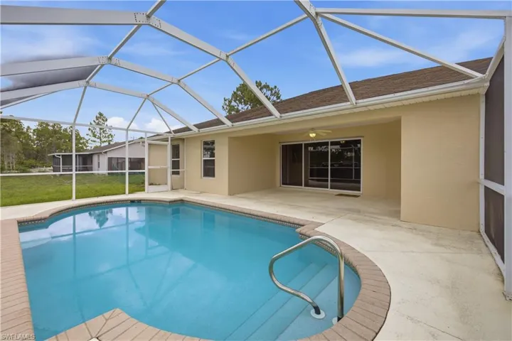 Screened pool enclosure featuring a concrete patio, curved pool steps with handrails, and a brick coping around the pool perimeter