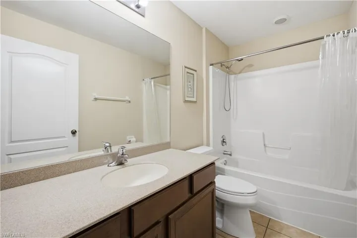 Full bathroom featuring a single vanity with a solid surface countertop, an undermount sink, and dark wood-finish cabinetry