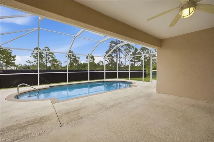 Screened enclosure featuring an elongated swimming pool with a handrail, substantial concrete decking, and a ceiling fan with integrated lighting