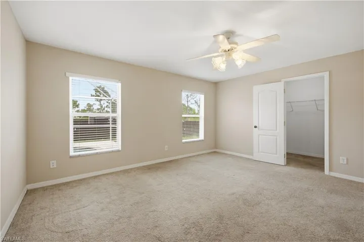 Carpeted interior space featuring two windows with blinds, a ceiling fan with integrated lighting, and a closet with wire shelving