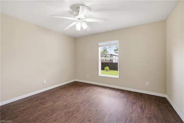 Interior room featuring wood-finish flooring, light-toned walls, a single window with blinds, a white ceiling fan with integrated lighting, and white baseboards