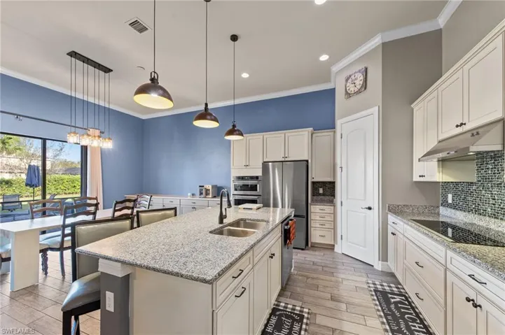 Kitchen with wood finish floors, light stone countertops, ornamental molding, backsplash, and a kitchen breakfast bar