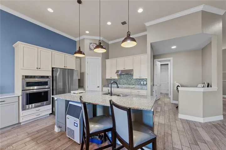 Kitchen featuring light stone countertops, a breakfast bar area, wood finish floors, crown molding, and backsplash
