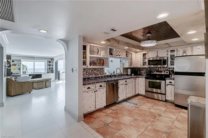 Kitchen featuring appliances with stainless steel finishes, arched walkways, light tile patterned flooring, ornamental molding, and tile counters
