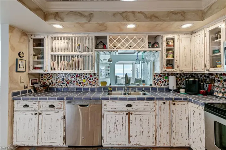 Kitchen with glass insert cabinets, tile countertops, appliances with stainless steel finishes, open shelves, and ornamental molding