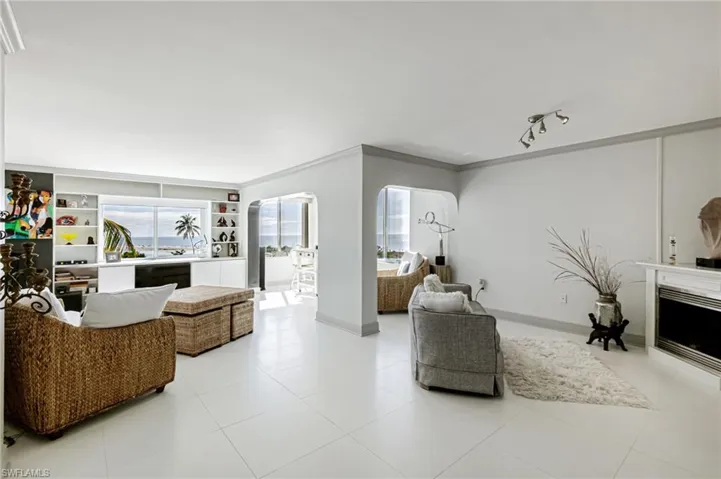 Living room featuring ornamental molding, a fireplace, arched walkways, tile patterned flooring, and built in shelves