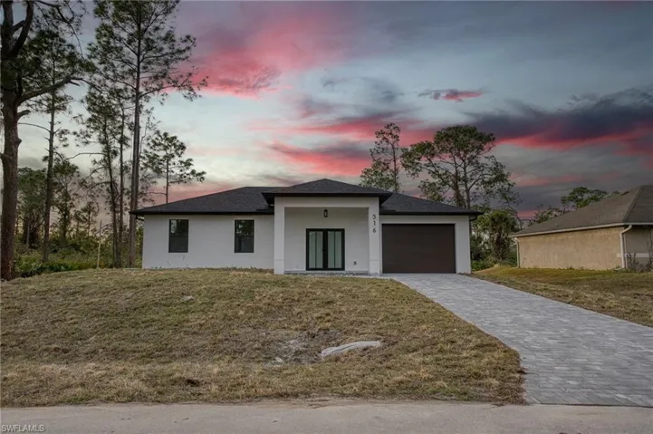 View of front of home with stucco siding, a lawn, decorative driveway, and a porch