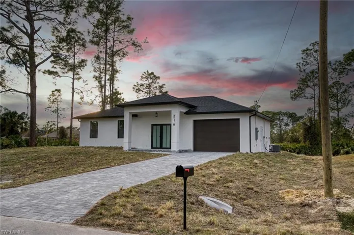 View of front of home with stucco siding, covered porch, decorative driveway, a garage, and a front lawn