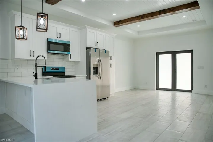 Kitchen featuring hanging light fixtures, appliances with stainless steel finishes, white cabinets, light stone countertops, and backsplash