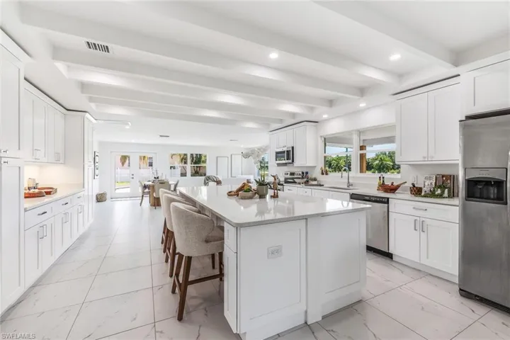 Kitchen featuring stainless steel appliances, light tile floors, white cabinetry, and beam ceiling