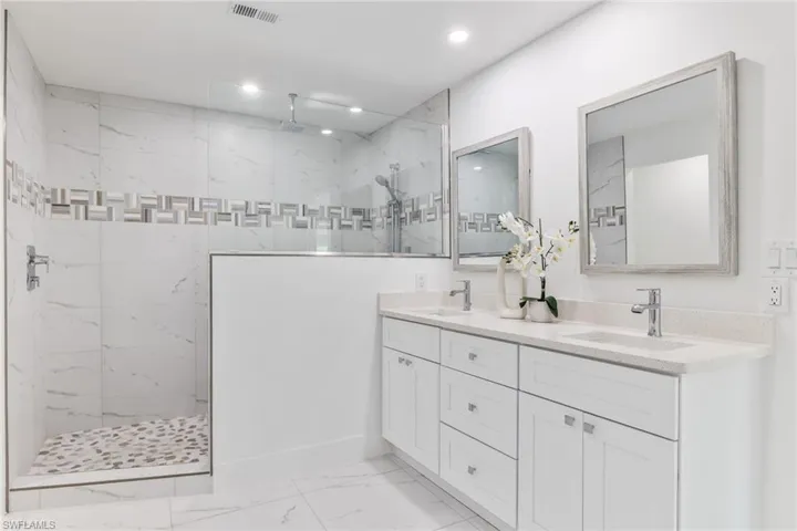 Owners suite bathroom with a tile shower, vanity with extensive cabinet space, dual sinks, and tile floors
