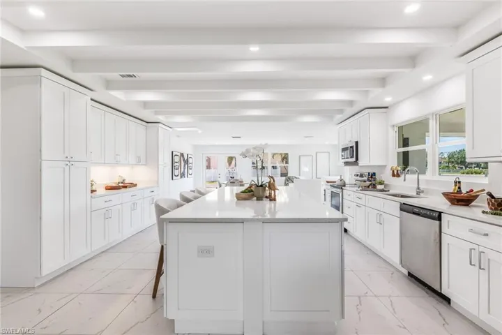 Kitchen with appliances with stainless steel finishes, white cabinets, beam ceiling, sink, and light tile floors