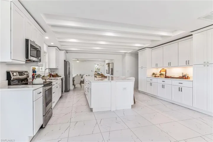 Kitchen featuring stainless steel appliances, white cabinets, beam ceiling, light tile floors, and oversized island