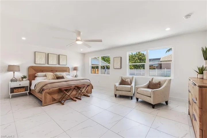 Owners suite bedroom featuring ceiling fan, natural lighting, light tile and room for private seating area