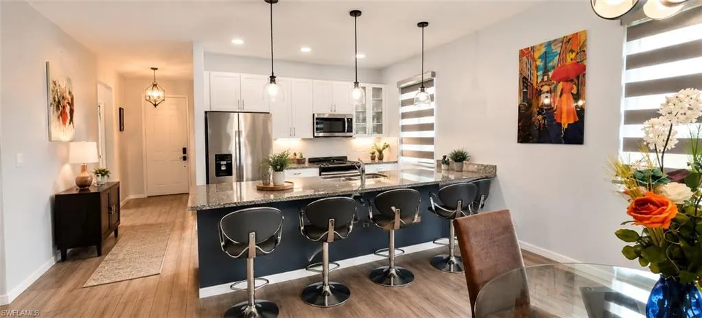 Open-concept kitchen featuring an oversized island with pendant lighting, stainless steel appliances, granite countertops, and wood-finish flooring