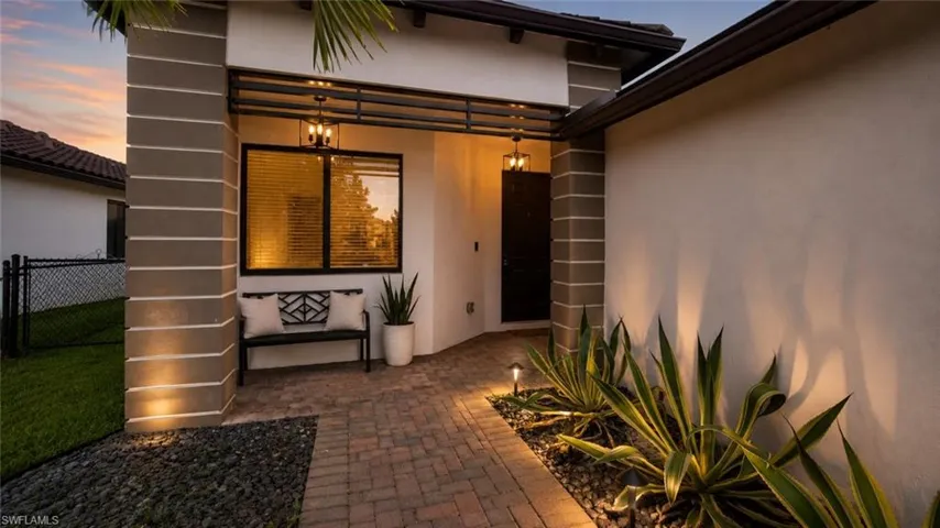 Inviting entry featuring a brick paver pathway, architectural columns, integrated exterior lighting, and a dark paneled entry door