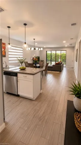 Open-concept living area featuring wood-finish flooring, a kitchen island with stone countertop, stainless steel appliances, and sliding glass doors
