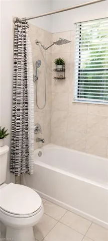 Bathtub with light-colored tile surround, featuring a shower/tub combination with a rain shower head and handheld sprayer