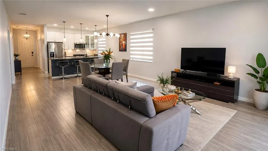 Open-concept living space featuring wood-finish flooring, a modern kitchen with stainless steel appliances, an island with seating, a dining area with a contemporary chandelier, and recessed lighting