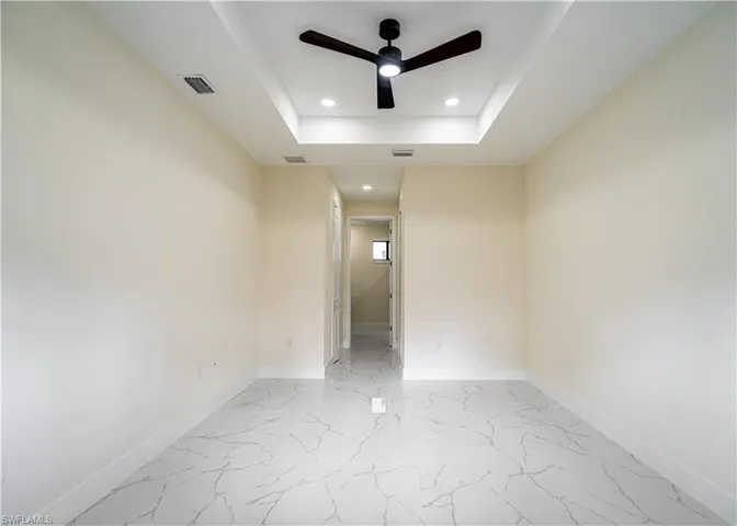 Spare room featuring a raised ceiling, a ceiling fan, recessed lighting, and light marble finish flooring